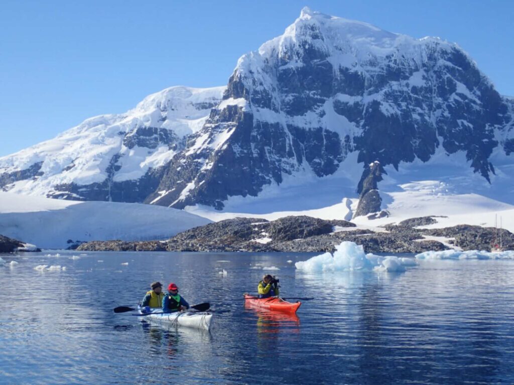 Person resting on a boat in Antarctica with glaciers and snowy mountains in the background.